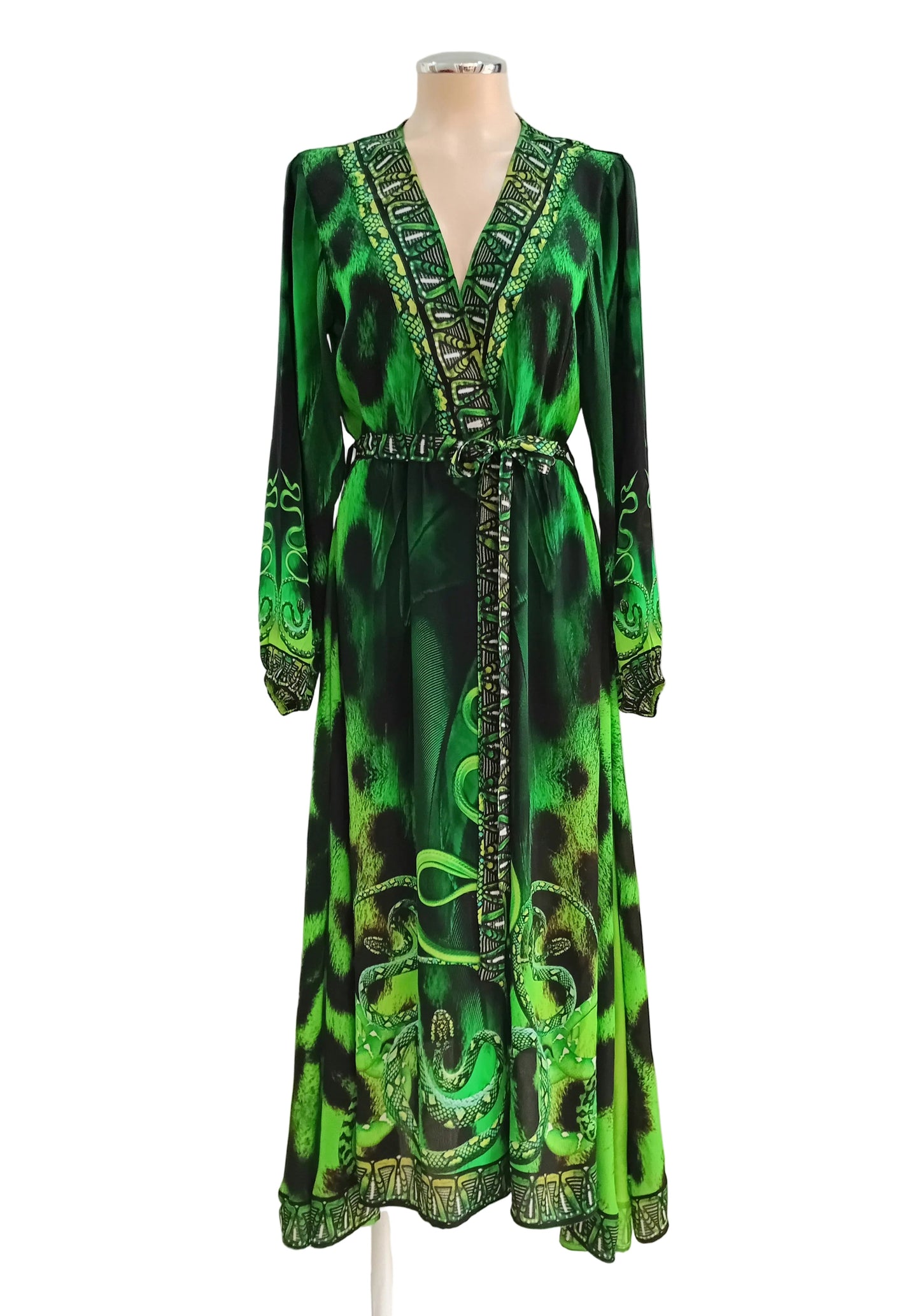Madusa Green and black patterned wrap dress against a white wall.