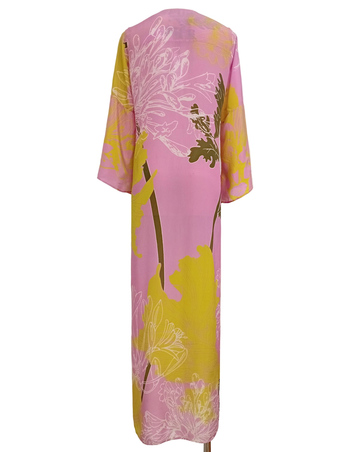 Tunic dress in a floral pink and lime yellow print against a white wall.