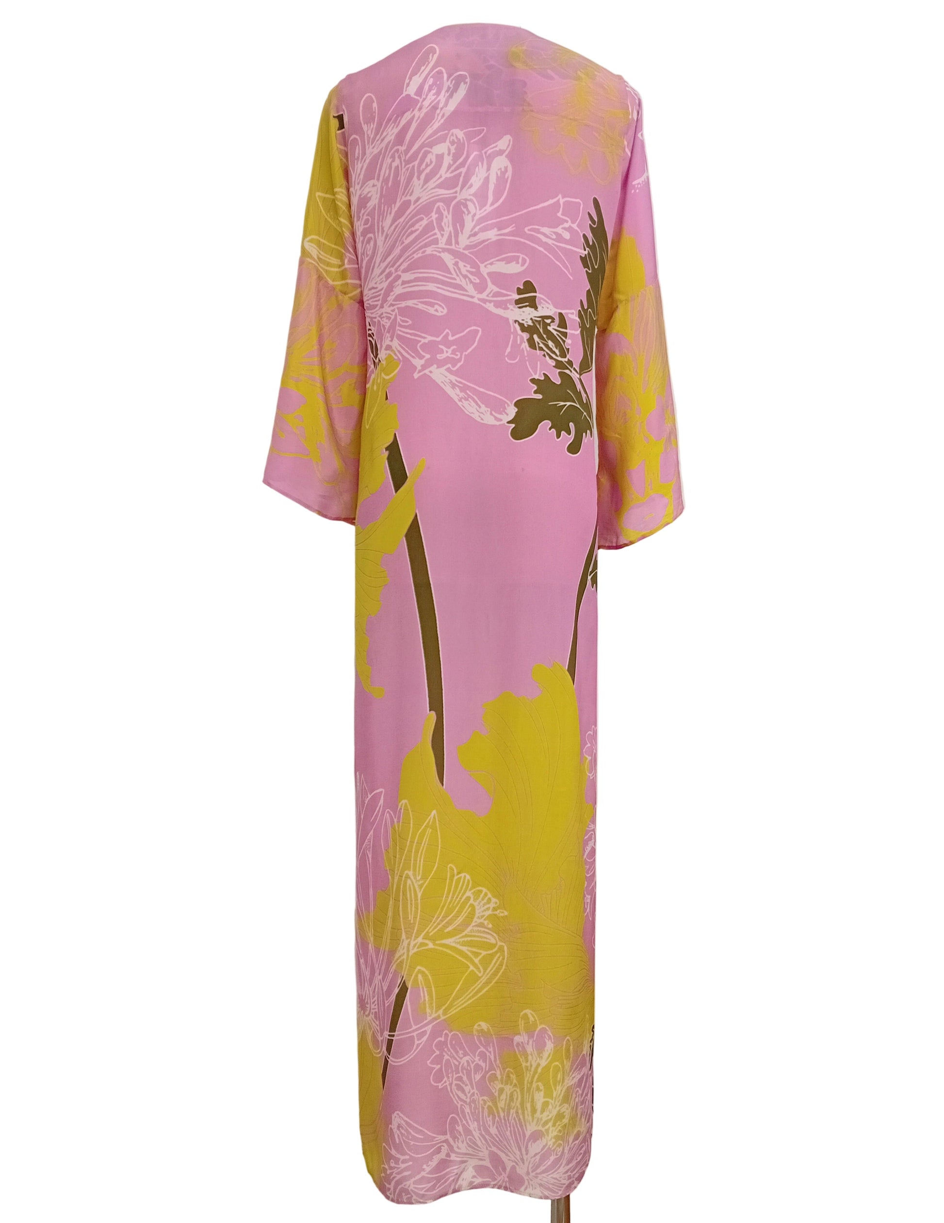 Tunic dress in a floral pink and lime yellow print against a white wall.